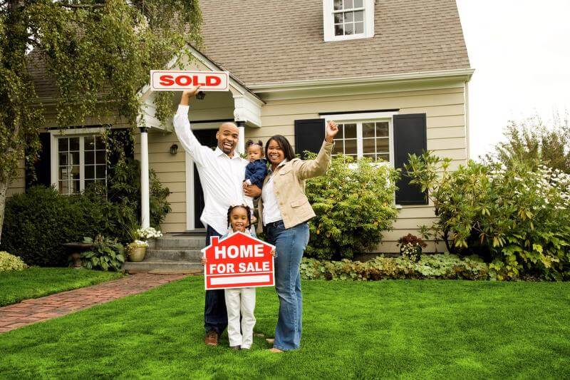 A family in front of a house with a sold sign.